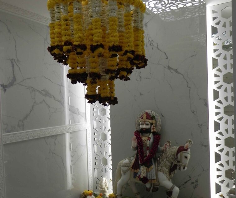 Home temple with marble-effect wall and yellow floral chandelier, pooja decor